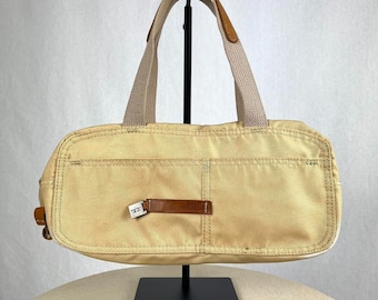 Könnte beinhalten: Eine beige Canvas-Tragetasche mit braunen Ledergriffen und Besätzen. Die Tasche hat eine große Tasche auf der Vorderseite mit dem aufgedruckten Wort "Diesel".