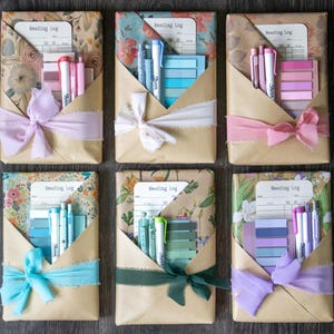 Flat lay of six beautifully wrapped blind date with a book packages in floral and kraft paper, each tied with colored ribbon and containing pastel stationery sets and a reading log.