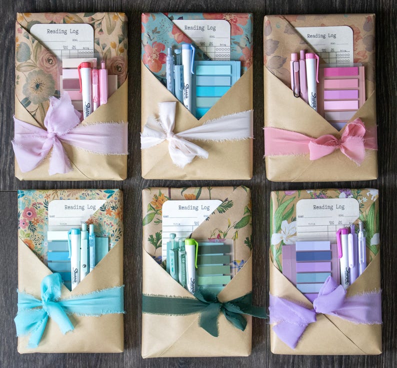 Flat lay of six beautifully wrapped blind date with a book packages in floral and kraft paper, each tied with colored ribbon and containing pastel stationery sets and a reading log.