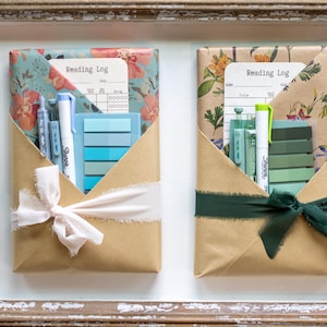 Pastel-themed blind date with a book packages featuring blue and green stationery items, floral kraft paper, and soft white or deep green ribbon, laid out in a wooden tray.
