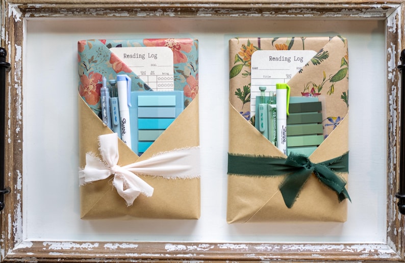 Pastel-themed blind date with a book packages featuring blue and green stationery items, floral kraft paper, and soft white or deep green ribbon, laid out in a wooden tray.