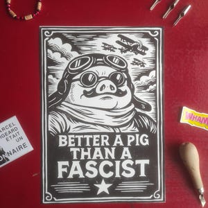 May include: Black and white linocut print featuring a pig wearing aviator goggles and a scarf, with the text "Better a Pig Than a Fascist." The image includes a star and airplanes in the background. Other items include a bracelet, tools, and stickers.