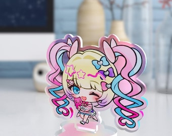 Puede incluir: Una colorida figura de acrílico de un personaje de estilo anime con cabello rubio, ojos azules y detalles en rosa y azul. El personaje sostiene un peluche rosa. La figura está sobre una base en forma de nube.