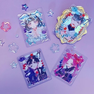 Peut inclure: Quatre porte-cartes en acrylique transparent avec des illustrations de personnages de style anime. Les cartes présentent divers motifs avec des accents bleus, rouges et roses. Des embellissements décoratifs en forme d'étoiles et de nuages entourent les cartes sur une surface violette.