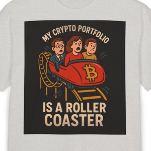 Puede incluir: Una camiseta gris con un gráfico cuadrado negro que presenta una imagen de dibujos animados de tres personas montando una montaña rusa con un símbolo de Bitcoin. El texto "My Crypto Portfolio Is A Roller Coaster" está impreso en blanco en el gráfico.