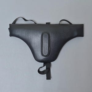 May include: A black leather saddle seat protector with a central padded section and attached straps. The protector has a curved shape and is designed to fit over a saddle seat. The straps are used to secure the protector.