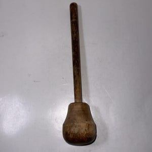 Könnte beinhalten: Ein Kartoffelstampfer aus Holz mit einem langen Stiel und einem runden, bauchigen Kopf.