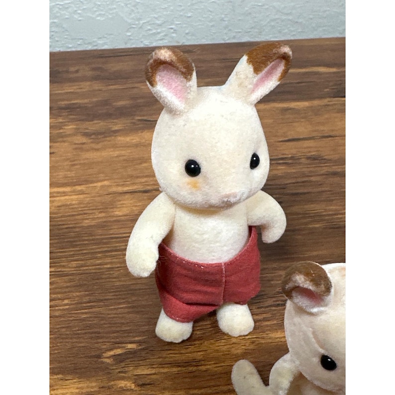 Pu&ograve; includere: Una piccola statuina di coniglio bianco con orecchie con la punta marrone e pantaloncini rossi. Il giocattolo ha occhi neri e un fard color pesca sulle guance. Il coniglio fa parte di una collezione di figurine di animali in miniatura.
