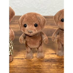 Op de afbeelding: Drie bruine speelgoedpuppy's met zwarte ogen staan op een houten oppervlak. De puppy's hebben een zachte, fluweelzachte textuur en staan. De afbeelding is goed verlicht en benadrukt de details van het speelgoed.