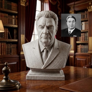 May include: A stone bust of a man in a suit and tie, with a serious expression. A framed black and white photograph of the same man is visible in the background. The bust is on a wooden table in a room with bookshelves and red curtains.