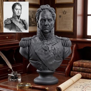May include: A dark grey bust sculpture of a military figure in a high-collared uniform with epaulettes, a sash, and a star-shaped medal on the chest. The figure has short, wavy hair and a stern facial expression, mounted on a circular pedestal base.