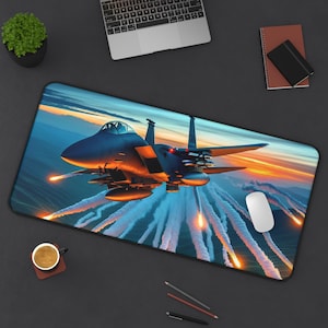 May include: A rectangular mousepad featuring a detailed illustration of a fighter jet in flight against a sunset sky. The jet is dark blue with orange accents, and trails of fire and smoke are visible.
