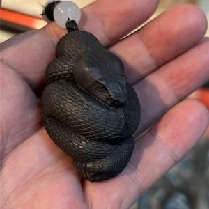 May include: A black wood carving of a snake curled up in a ball. The carving is detailed and realistic, with scales and a textured surface.