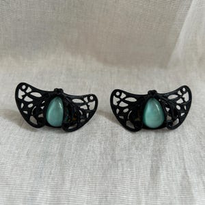 Pode incluir: Um par de brincos de filigrana preta com uma pedra azul claro em forma de lágrima no centro de cada brinco.