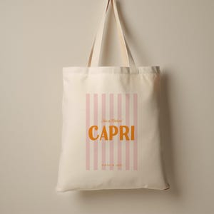 May include: A white canvas tote bag with pink and white stripes. The bag has the text "Tina & Michael Capri" in orange letters and the date "August 18, 2024" in smaller black letters.