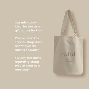 May include: A beige mini tote bag with a cream-colored handle. The bag has the word "mini" printed on it, along with the dimensions 9 x 12 inches and 15-inch handles. Text on the left side provides additional details.