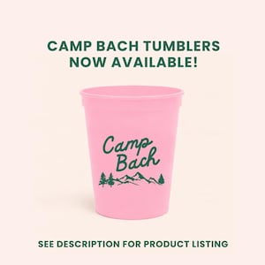 May include: A pink plastic tumbler with the words "Camp Bach" in a green script font, along with a mountain and tree graphic. The text "CAMP BACH TUMBLERS NOW AVAILABLE!" is at the top. The bottom text reads "SEE DESCRIPTION FOR PRODUCT LISTING".