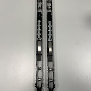 Puede incluir: Dos rieles negros y plateados para puertas correderas. Cada riel es largo y rectangular con múltiples componentes plateados y negros. Los rieles están diseñados para permitir que una puerta se deslice. Los rieles están colocados uno al lado del otro.