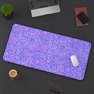 May include: A rectangular desk mat with a vibrant, abstract pattern in shades of purple, blue, and white. A white computer mouse rests on the mat. The mat is surrounded by a laptop, a small potted plant, a notebook, and a cup of coffee.