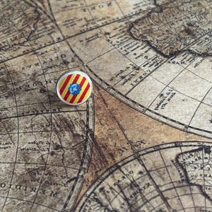 May include: A circular badge with a white edge, displaying red and yellow stripes and a blue emblem, sits on a vintage map. The map is sepia-toned, showing continents and oceans with detailed lines.