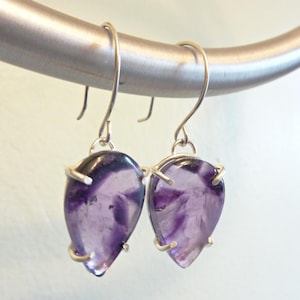 May include: A pair of silver earrings with purple amethyst teardrop-shaped stones.