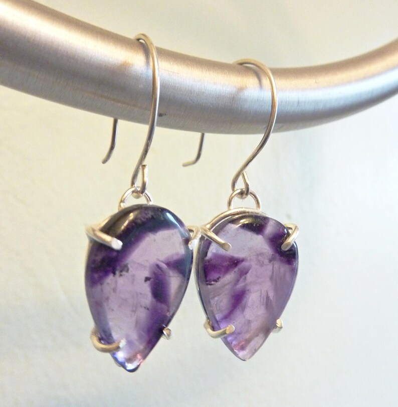 May include: A pair of silver earrings with purple amethyst teardrop-shaped stones.