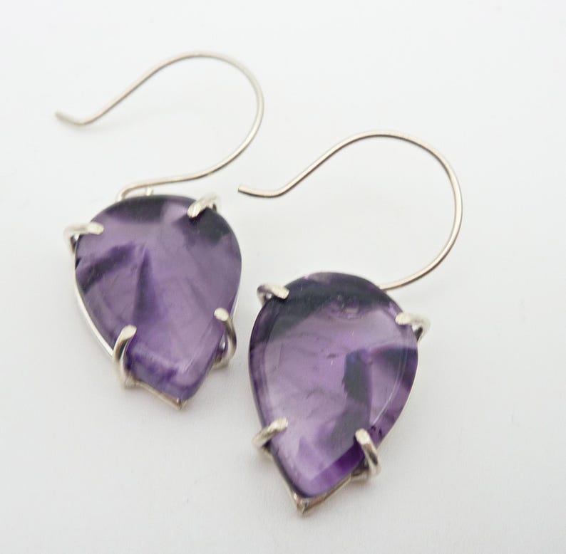 May include: A pair of silver dangle earrings with purple amethyst stones. The stones are faceted and have a teardrop shape.