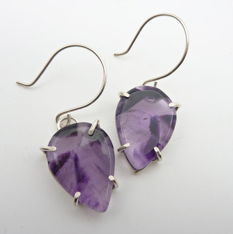 May include: A pair of silver earrings with purple amethyst teardrop-shaped stones set in a bezel setting.