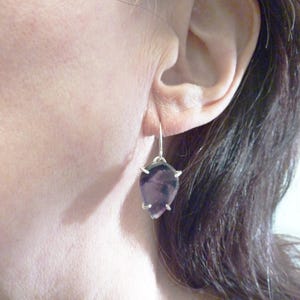May include: A pair of silver dangle earrings with a teardrop-shaped purple gemstone. The earrings have a simple design and are perfect for everyday wear.