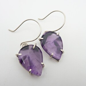 May include: A pair of silver dangle earrings with purple teardrop-shaped gemstones.