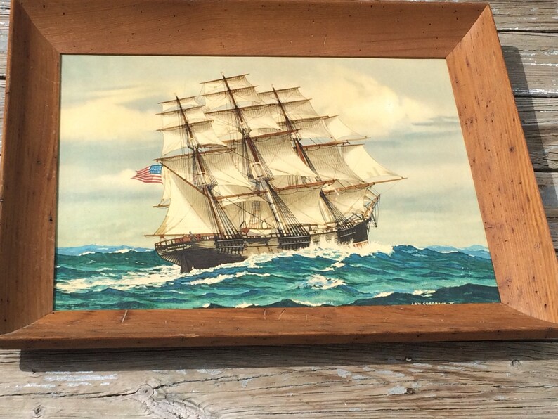 May include: A framed painting of a large sailing ship with white sails and a blue and red American flag. The ship is sailing on a blue ocean with white waves.