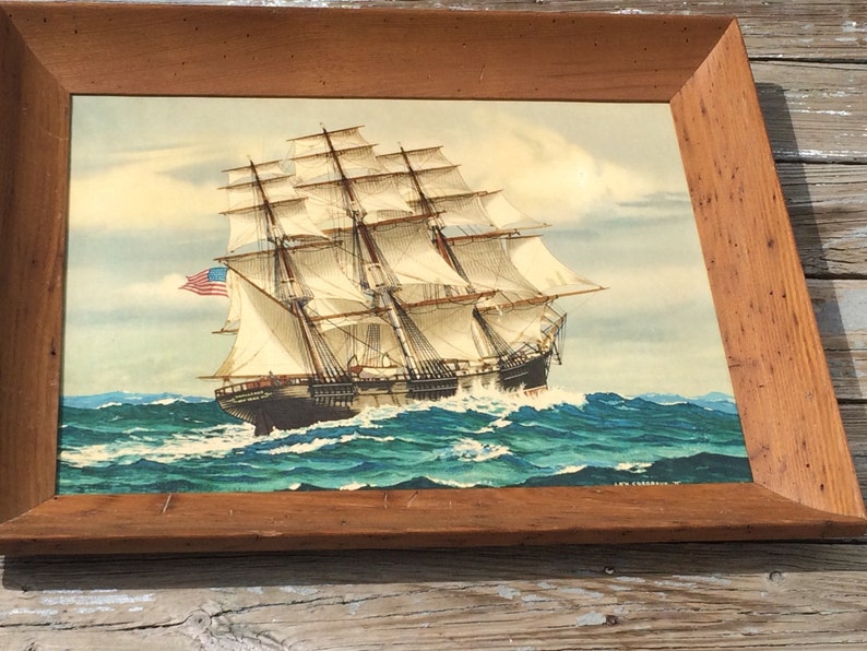 May include: A framed painting of a large sailing ship with white sails, a dark hull, and an American flag flying from the mast. The ship is sailing on a blue and green ocean with white waves.