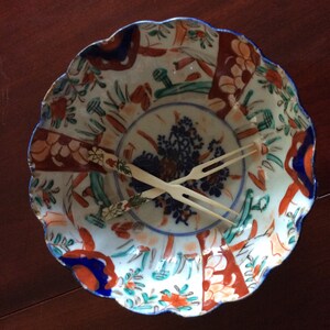 May include: A white porcelain bowl with a scalloped rim and a colorful floral pattern. Two ivory chopsticks are resting inside the bowl.