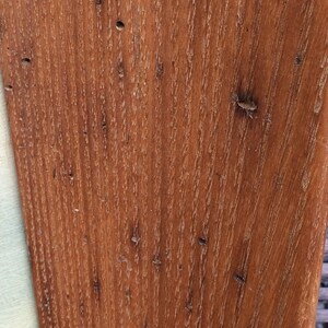 May include: Close-up of a wood grain surface with a reddish-brown color. The wood has a natural, rustic look with knots and grain patterns.