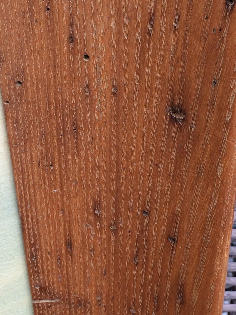 May include: Close-up of a wood grain surface with a reddish-brown color. The wood has a natural, rustic look with knots and grain patterns.