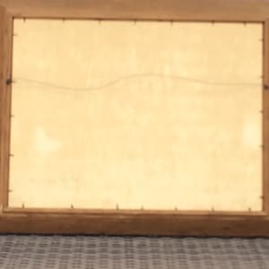 May include: A wooden picture frame with a light brown finish. The frame is empty and has a wire hanger on the back.