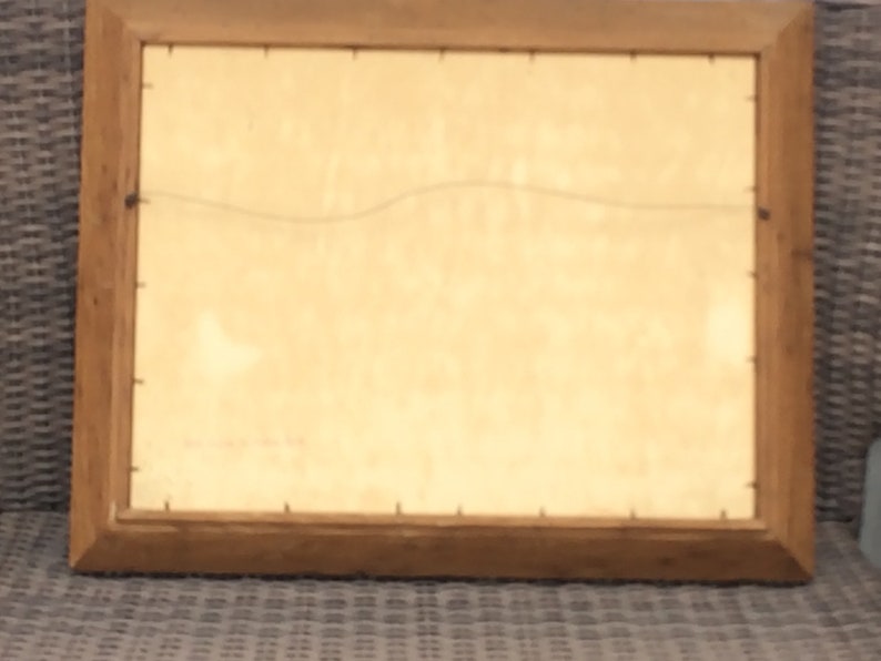 May include: A wooden picture frame with a light brown finish. The frame is empty and has a wire hanger on the back.