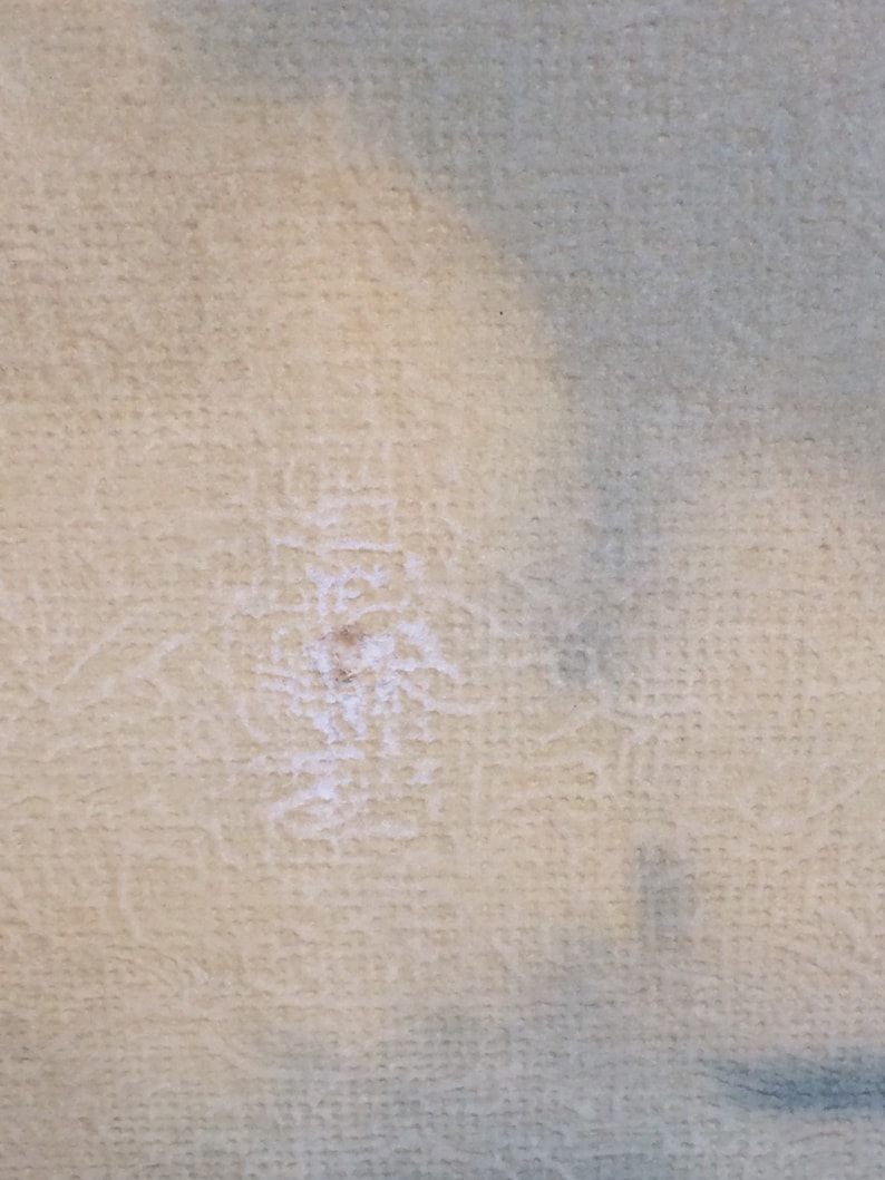 May include: Close-up of a light beige textured fabric with a small white stain in the center.