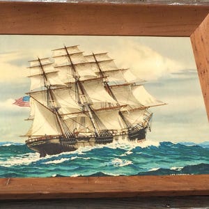 May include: A framed painting of a large sailing ship with white sails and an American flag, sailing on a blue ocean with whitecaps.
