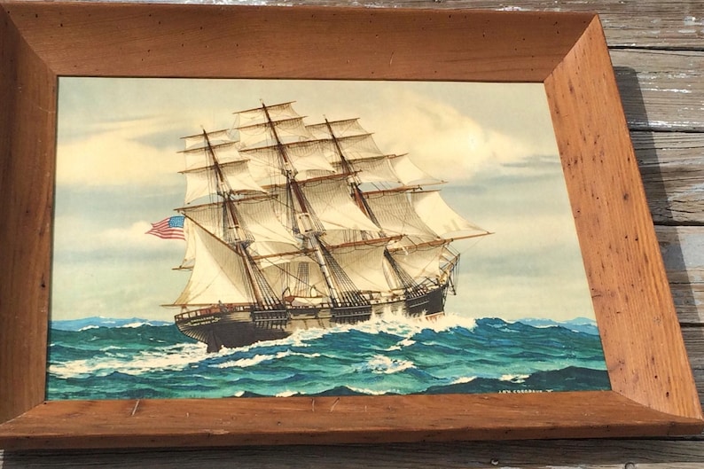 May include: A framed painting of a large sailing ship with white sails and an American flag, sailing on a blue ocean with whitecaps.