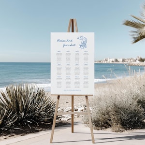 Puede incluir: Un cartel rectangular blanco de distribución de asientos para bodas sobre un caballete de madera. El cartel presenta texto azul que dice Please find your seat, un dibujo lineal de una silla y sombrilla de playa, y doce columnas de nombres.