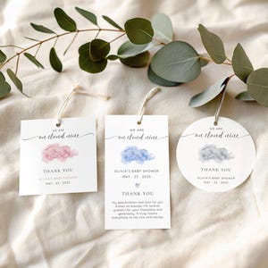 May include: White baby shower favor tags with watercolor cloud designs in pink, blue, and gray. Each tag reads "We are on cloud nine" and includes the text "Thank You" and the baby shower date.