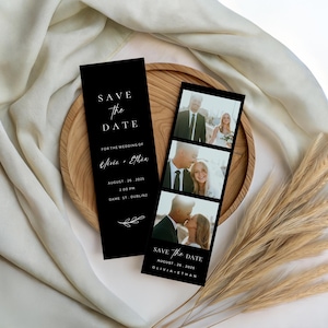 Op de afbeelding: Zwarte trouwkaarten met de tekst "Save the Date". Eén kaart bevat de tekst "Save the Date" en huwelijksdetails. De andere kaart heeft een fotostrip met drie afbeeldingen van het paar. De kaarten liggen op een houten dienblad.