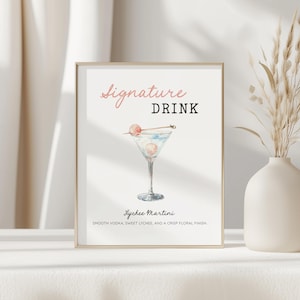 May include: Framed print featuring a watercolor illustration of a Lychee Martini cocktail. The text reads "Signature Drink" in pink script and black block letters. Below the cocktail, the text says "Lychee Martini" and describes the drink.