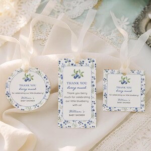 Könnte beinhalten: Drei Babyparty-Geschenkanhänger mit Blaubeer-Motiv. Die Anhänger haben einen weißen Hintergrund mit blauem Blumenmuster und dem Text "Thank You berry much". Jeder Anhänger ist mit einem weißen Band gebunden.