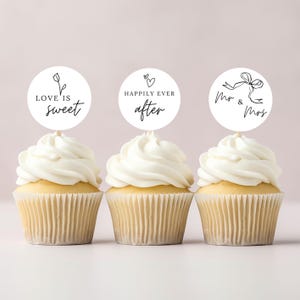 Op de afbeelding: Drie cupcakes met witte frosting en ronde toppers. De toppers hebben zwarte tekst en ontwerpen met de tekst "Love is sweet", "Happily ever after" en "Mr & Mrs". De cupcakes hebben een lichtbruine basis.