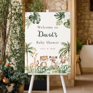 May include: A white easel sign with the text "Welcome to David's Baby Shower" and the date July 8, 2025. The sign features watercolor illustrations of jungle animals, palm trees, and tropical leaves.