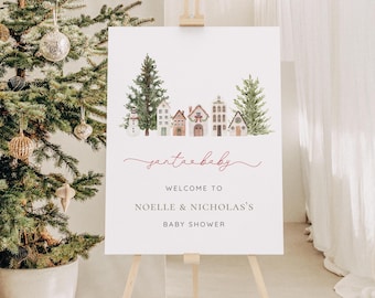 May include: A white sign on an easel with a watercolor illustration of a winter village scene. The sign reads "santa baby" in cursive, followed by "Welcome to Noelle & Nicholas's Baby Shower."