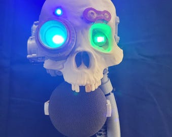 May include: A white skull-shaped mask featuring a glowing blue light on the forehead, a large circular eyepiece with a bright green light, and a second eye socket with a green light. A grey spherical speaker is attached below the jaw with a hose.