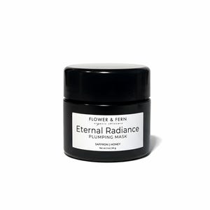 May include: A black jar of Eternal Radiance Plumping Mask by Flower & Fern. The jar has a white label with the product name and ingredients: Saffron and Honey. The net weight is 2 oz.